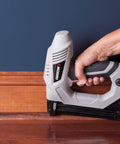 Hand holding Heavy Duty Electric Brad Nailer for Trim and Framing Projects, Beast Nail Gun pressing baseboard.