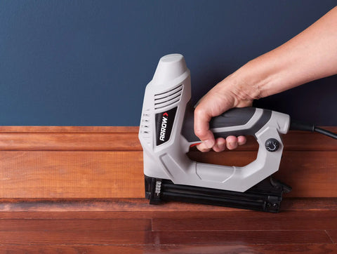 Hand holding Heavy Duty Electric Brad Nailer for Trim and Framing Projects, Beast Nail Gun pressing baseboard.