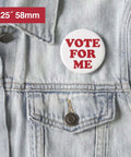 White 58mm blank button badge with red VOTE FOR ME text, pinned to a denim jacket.