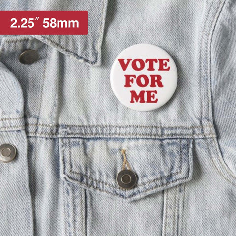White 58mm blank button badge with red VOTE FOR ME text, pinned to a denim jacket.