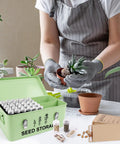 Gardener potting plant with open 60 Slot Metal Seed Storage Organizer with lid, safety locks, envelopes, and labels on table