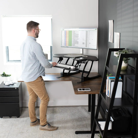 Man using 43 Inch Corner Electric Height Adjustable Desk Riser For Dual Monitors, Sit To Stand Tabletop Converter With USB Port