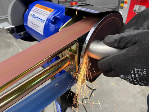 Hella Compatible 2X48 Belt Grinder Attachment Converts Standard Bench Grinder Into Rock Solid Vertical Or Horizontal Grinding Rig Featuring No Sweat Quick Change Tension System with sparks during use.