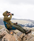 Man sitting on rocks using HEX 2.0 No Frills Outdoor Chair For Camping And Stadium Seating With All Terrain Comfort Adjustable Straps