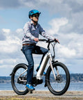 Person riding an electric mountain bike by the ocean in casual attire on a sunny day