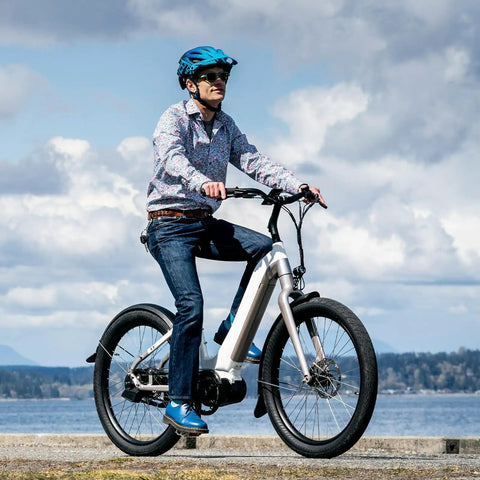 Person riding an electric mountain bike by the ocean in casual attire on a sunny day