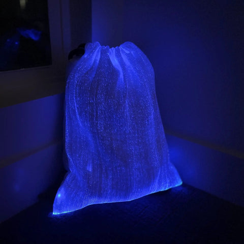 LED Fiber Optic Drawstring Backpack With 11 Lighting Modes Including 7 Colors And 4 Flash Patterns Lit Party Ready Glow For Festivals Raves And EDM Shows Plus Anti Theft Pocket And 40 By 34 Cm glowing in blue in a dark room