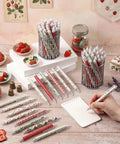108 Pink Strawberry Themed Retractable Ballpoint Pens Bulk Set With 9 Styles Glittery, laid out around a notebook with decorative setting