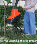 Person using Beast 1800W Electric Wood Chipper Shredder for yard cleanup, cutting branches near a tree.