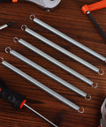 Six zinc-plated extension springs with dual hooks, 3/8 x 6-1/2 in, top-down view with pliers and saw.