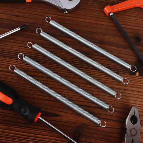 Six zinc-plated extension springs with dual hooks, 3/8 x 6-1/2 in, top-down view with pliers and saw.