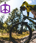 Cyclist on mountain trail with Durable Nylon Mountain Bike Pedals With DU Bearings Lightweight Platform Pedals in purple.