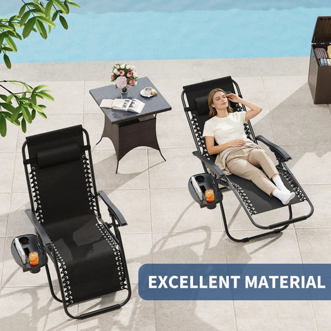 Woman relaxing on Zero Gravity Lounge Chairs Set Of 2 with Pillow and Cup Holder Tray, black, on a patio next to a table.