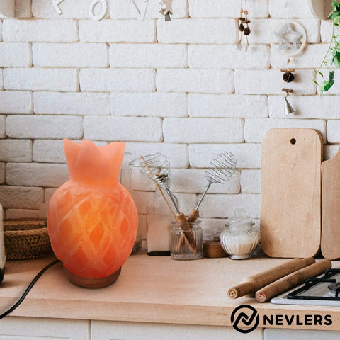 Pineapple-shaped Himalayan salt lamp with warm glow on kitchen counter, surrounded by utensils and decor.