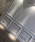 Modern interior wall with geometric panel design and spotlight, against a hardwood floor backdrop.