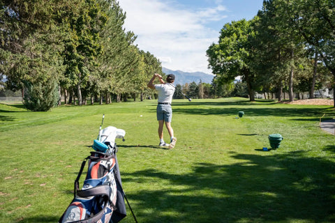 Golfer practicing swing on course, golf bag in foreground with Pin Point Golf Swing Tempo Trainer And Warm Up Club.