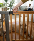 Woman opening Oak Wood And Metal Baby And Pet Gate For 36 To 60 Inch Openings, 30 Inch Tall, dog laying behind it, man on sofa