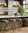Modern kitchen with gold pendant lights, wooden bar stools, and green cabinets showcasing restoration supplies.