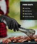 TitanFlex black nitrile gloves, 6-mil textured; worn by hand using metal tongs over grilled meat.