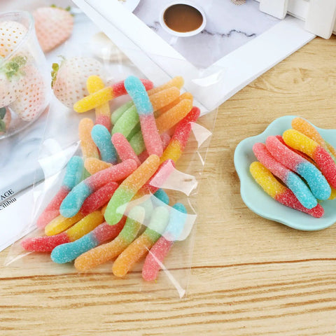 300 Count 4x6 Inch Self Adhesive Cellophane Bags 2.8 Mil Clear Plastic Bags filled with colorful gummy worms on a wooden table