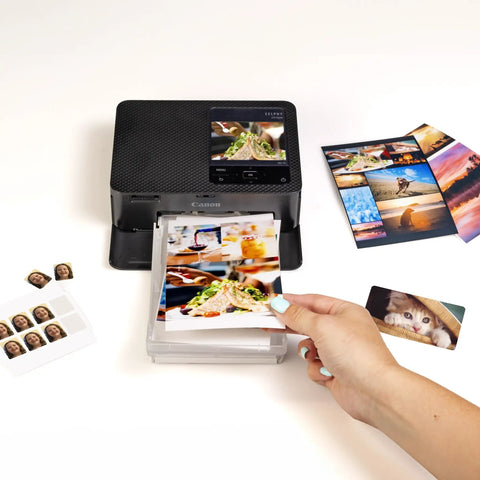 Selphy CP1500 Wireless Photo Printer In Black Ultra Portable Mini Printer With WiFi And Smartphone Connectivity on table with photos