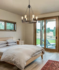 Farmhouse Wagon Wheel Chandelier Eight Light Rustic Round Metal Fixture for Dining Room Living Room Bedroom and Foyer with Natural Rope Accents and Weathered Wood Look for a Warm Cozy Rustic Aesthetic hanging in a bedroom.