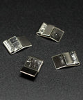 Four small silver metal clips on a dark surface, arranged in a scattered pattern.