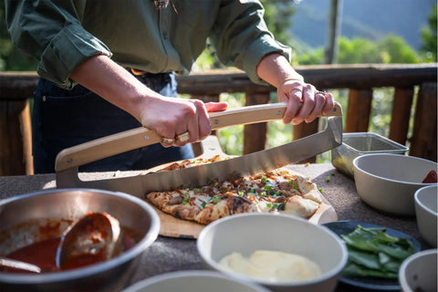 Person using Pi Pizza Rocker Cutter Pro For Effortless Slicing Of Thin Or Thick Crust Pizza With Stainless Steel Rocker Blade And Bamboo Handles