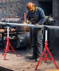 Pipe jack stands, red steel, adjustable height, front view supporting a welded metal pipe in factory setting