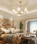 Smooth Operator 6 Light Brass Gold Chandelier With White Fabric Shades above an elegant bedroom setting with plush bedding.