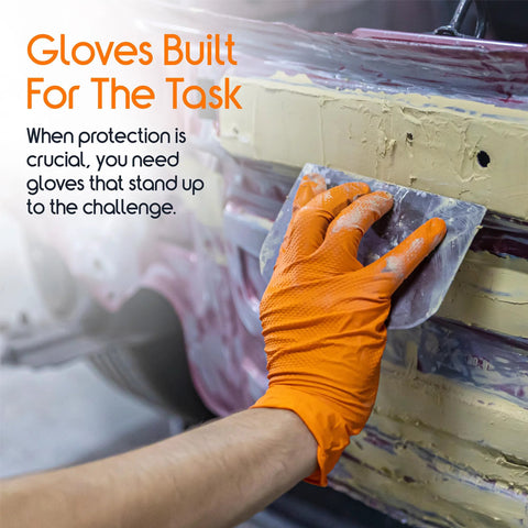 Close-up of orange nitrile disposable glove (small) on hand holding a metal scraper against a workshop surface.