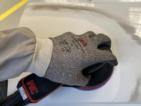 Hand holding a sander with 3M Cubitron II Hookit Abrasive Disc on a smooth surface for auto work.