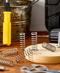 Six stainless steel coil springs, 1/2 in by 1-1/2 in, on a wooden workbench.