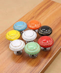 Totally Groovy Blue Mushroom Ceramic Cabinet Knobs, 6 Pack of Glossy Round Drawer Pulls for Dresser and Wardrobe, 1.38 Inch Diameter, Smooth Polish, 3 Screw Sizes Included, Home Makeover Essential multi-colored ceramic knobs on a wooden surface.