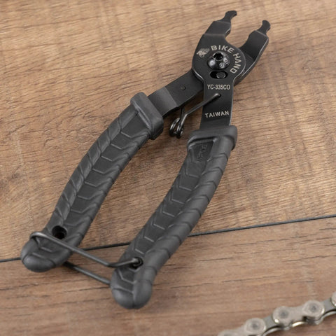 Bike Chain Master Link Pliers 2 In 1 Tool For Easy No Sweat Quick Link Removal And Replacement Compatible With Shimano Sram KMC Chains All Brands MTB Road Use Everyday, black rubber grip handles on wooden surface.