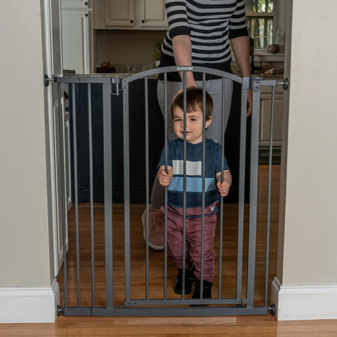 Child standing behind gray Extra Tall Decor Safety Gate for Kids and Pets in 28-38.25 inch openings, installed in doorway