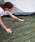 Woman setting up Rugged Camo Tarp 20ft By 30ft Heavy Duty Outdoor Shelter With 6 Oz Material, 12 Mil Thickness, near a tent