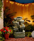 Six Tier Cascading Rock Outdoor Water Fountain With Lights for garden patio setup, placed on a deck with surrounding plants, 24.4 inch high