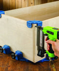 Blue Three Quarters Inch Corner Clamp Clips Four Pack For Woodworking securing corner of wooden box with nail gun in use.