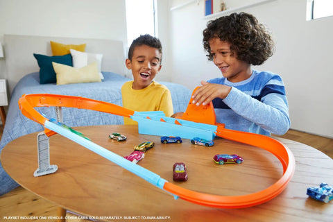 Kids playing with Rapid Raceway Champion Drag Race Track Set With Start Gate For Quick Countdown Side By Side One On One Racing Multi Car Launcher Connects To Other Sets Includes 1 64 Scale Car For Realistic Speed Play on a table.