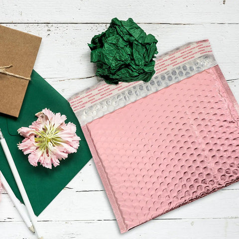 Pink 25 Pack Self Seal Bubble Mailer Envelopes 25x20cm on wooden table with green paper and flower