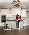 56 to 130 Inch Wide Baby Gate and Play Yard in kitchen, mom holds baby, child plays on floor, wall-mounted gate setup