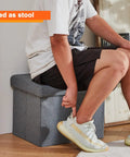 Person sitting on Storage Ottoman Footrest Stool With Hidden Storage, Foldable Footstool Bench For Living Room, 17 x 13 x 13 in, gray