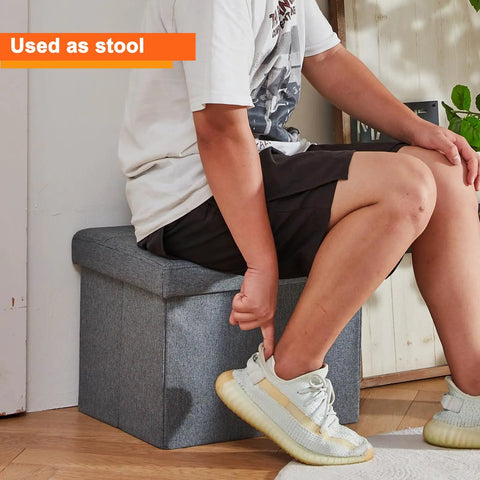Person sitting on Storage Ottoman Footrest Stool With Hidden Storage, Foldable Footstool Bench For Living Room, 17 x 13 x 13 in, gray