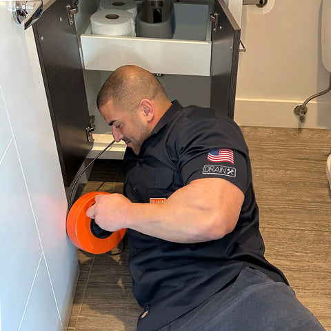 Person using Pro Grade Heavy Duty 25 Foot Steel Drum Auger Drain Snake Kit With One Quarter Inch Cable For One And A Quarter To Three Inch Drains under sink
