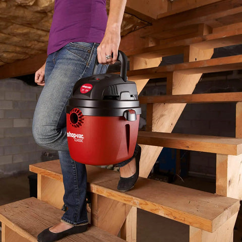 Person carrying 1.5 Gallon 2.0 Peak Wet Dry Vacuum For Quick Cleanups At Home, Garage, Or Vehicle, with collapsible handle.