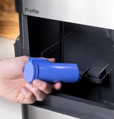 Person holding a blue filter for the Genuine Game Changing Nugget Ice Maker With Smart Wifi App And Built In Scale Fighting Filter Makes Hella Crisp Chewable Pellet Ice Fast Comes With Handy Scoop Sleek Stainless Build.