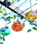 Set Of 3 Small Blown Glass Hummingbird Feeders For Outdoors Hanging With 2 Flower Feeding Ports 3 Inch Glass Hummingbird Feeders Garden Decor For Outside in colorful designs, hanging in a garden setting.