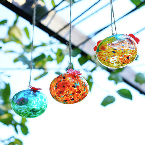 Set Of 3 Small Blown Glass Hummingbird Feeders For Outdoors Hanging With 2 Flower Feeding Ports 3 Inch Glass Hummingbird Feeders Garden Decor For Outside in colorful designs, hanging in a garden setting.