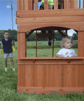 Children playing on Atlantis Cedar Wood Swing Set With Wave Slide And Raised Clubhouse Featuring Rock Wall, Belt Swings, Balcony.